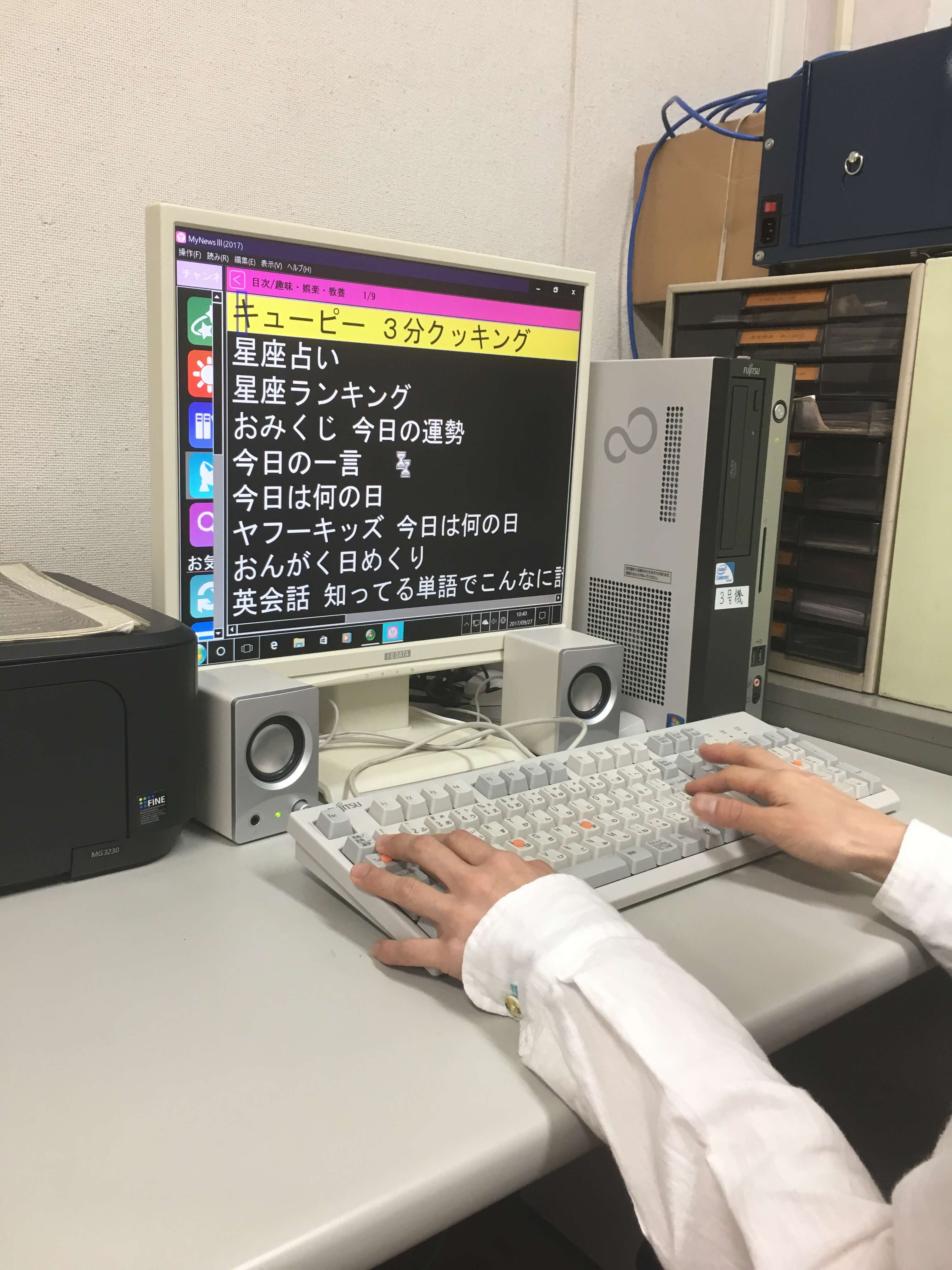 「机の上のパソコンの画面に白黒反転した目次画面が出ていてキーボードで操作をしようとしています。」